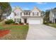 Charming two-story home with tan siding, dark shutters, a well-manicured lawn, and an attached two-car garage at 210 Sabal Palmetto Ct, Moncks Corner, SC 29461