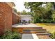 Backyard with a wood patio that has a table and chairs on a rug, with a side view of the brick home at 1756 Mchenry Ave, Charleston, SC 29412