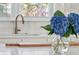 Close-up of a kitchen sink with a bronze faucet, white countertops, and blue flowers in the foreground at 1756 Mchenry Ave, Charleston, SC 29412