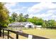 A white barn sits amidst a lush green field, framed by a black fence and trees under a partly cloudy sky at 5276 7Th Green Dr, Hollywood, SC 29449