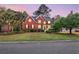 Inviting two-story red brick home with a manicured front lawn, mature trees, and a charming front porch at 1185 Out Of Bounds Dr, Summerville, SC 29485