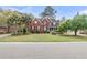 Inviting two-story red brick home with a manicured front lawn, mature trees, and a charming front porch at 1185 Out Of Bounds Dr, Summerville, SC 29485