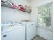 Bright laundry room with white washer, dryer, storage shelf, and natural light from the window at 5009 W Liberty Park Cir, North Charleston, SC 29405