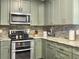 Modern kitchen features stainless steel appliances, stone backsplash, and stylish green cabinets at 8810 Gilston Ln, North Charleston, SC 29420