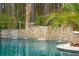 Beautiful waterfall feature cascading into this property's backyard pool, lined with palm trees and a dense forest backdrop at 184 Clearblue Loop, Summerville, SC 29486