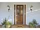 Close-up of a wood front door with glass panels, flanked by plants and sconce lighting at 2 Wills Way, Isle of Palms, SC 29451