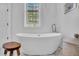 Soaking tub under a decorative window with an ornate glass design, complemented by stylish stool and basket at 2340 Salt Wind Way, Mount Pleasant, SC 29466