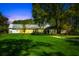Exterior view of a well-lit home with lush green lawn and mature trees at dusk at 3060 Bohicket Rd, Johns Island, SC 29455