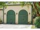 A carriage house with green arched doors, sconces, and a neutral stucco exterior is set off by mature, lush landscaping at 2 Leone Ln, Hanahan, SC 29410