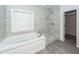 Bright bathroom features a jetted tub, a tiled walk-in shower, gray tiling, and a window at 5496 Clearview Dr, North Charleston, SC 29420