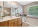 Bright bathroom featuring a soaking tub with tile surround, double sink vanity, and large window at 9316 Sweetbay Ct, Ladson, SC 29456
