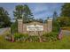Community entrance featuring a brick sign, colorful flowers, manicured lawn, and flagpole surrounded by American flags at 4403 Wild Thicket Ln, North Charleston, SC 29420