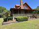 Log cabin home exterior with red metal roof, stone chimney, covered porch, and landscaped yard at 6935 Hickorynut Ln, Ravenel, SC 29470