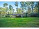 Spacious backyard featuring a brick home, covered patio, lush lawn, and tall pine trees, ideal for outdoor activities at 112 Furlong Rd, Summerville, SC 29483