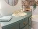 Close-up on the green bathroom vanity with a white sink, gold faucet and exposed brick wall at 114 California Ave, Moncks Corner, SC 29461