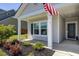View of a cozy front porch with an American flag, lush landscaping, and a black front door at 117 Camellia Bloom Dr, Moncks Corner, SC 29461