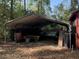 Exterior shot of the covered outbuilding with red accents, in a wooded setting at 1020 Welles Ln, Walterboro, SC 29488