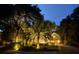 Exterior home view at night, featuring landscape lighting, mature trees, and a welcoming driveway at 126 Sparrow Dr, Isle of Palms, SC 29451