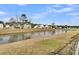 Backyard pond view, showcasing the serene water feature bordered by green grass and neighborhood houses with trees in the background at 1516 Mandarin Ct, Summerville, SC 29483