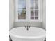 Close-up of modern soaking tub positioned below double window with white blinds and trim at 2636 Colonel Harrison Dr, Johns Island, SC 29455