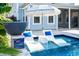 Relaxing in-pool lounge chairs with blue pillows and umbrella for shade, beside lush, tropical landscaping at 282 Great Lawn Dr, Summerville, SC 29486