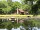 A beautiful log home featuring a stone chimney, large windows, and a deck, with a tranquil pond in the foreground at 5354 Ceva Dr, Hollywood, SC 29449