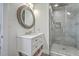 Bathroom with a round decorative mirror, white vanity, and seamless glass shower with tiled surround at 169 Jackson St, Charleston, SC 29403