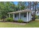 Charming blue cottage with a covered porch, lush greenery, and a well-maintained yard at 228 Dogwood Trl, Harleyville, SC 29448