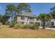 Charming home features a light-colored exterior, inviting porch, and verdant surroundings, blending comfort with nature's beauty at 60 Rice Ln, Edisto Beach, SC 29438