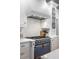 Close-up of the blue gas range, with custom hood, marble countertops, and white backsplash at 1081 Groves Manor Ct, Mount Pleasant, SC 29464
