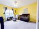 Bright bedroom with yellow walls, ceiling fan, and a crib with dark wood trim beside a grey armchair and ottoman at 5276 Copley Cir, Summerville, SC 29485