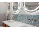 Bathroom with double sink vanity, modern faucets, blue tiled backsplash, and illuminated round mirrors at 1673 Mcclain St, Charleston, SC 29407