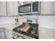 Close up of gas range top, microwave, subway tile backsplash and white countertop with gray cabinets at 533 Richfield Way, Summerville, SC 29486