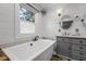Bright bathroom with a tub next to a window, shiplap walls, gray vanity and round mirror at 699 Castle Pinckney Dr, James Island, SC 29412
