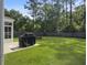 Well-manicured backyard with an outdoor grill, firepit, green lawn, and tree-lined fence at 2016 Elvington Rd, Johns Island, SC 29455