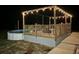 Backyard pool with wooden deck and an illuminated pergola adorned with hanging string lights on a quiet night at 1044 Towhee Ln, McClellanville, SC 29458