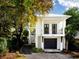 Inviting two-story house featuring a dark garage door, a small balcony, and lush landscaping, surrounded by large trees at 124 Charleston Blvd, Isle of Palms, SC 29451