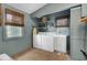 Well-lit laundry room with white washer and dryer, shelving, sink, windows with shades, and a woven rug at 418 W Carolina Ave, Summerville, SC 29483