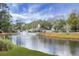 A scenic pond featuring a water fountain, surrounded by lush greenery, a clubhouse, and serene landscaping at 7896 Montview Rd, North Charleston, SC 29418