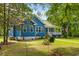 Picturesque blue home nestled in lush greenery, featuring a cozy porch and manicured lawn at 6035 Bay Pond Rd, Ravenel, SC 29470