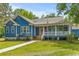 Charming blue home features a covered porch and an American flag displayed in the landscaped front yard at 6035 Bay Pond Rd, Ravenel, SC 29470