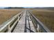 Rustic wooden boardwalk stretching into the distance, surrounded by marshland and a clear blue sky at 148 Cowrie Ct, Mount Pleasant, SC 29464