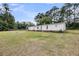 View of the side and backyard with lush green grass, trees, and a firepit at 5056 Red Oak Rd, Cottageville, SC 29435