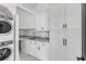 Bright laundry room featuring stacked washer/dryer, marble counters, and white cabinets with modern, dark hardware at 853 Whispering Marsh Dr, Charleston, SC 29412