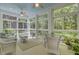 Bright sunroom with natural light from many windows, wicker furniture, ceiling fans, and views of a lush, wooded backyard at 4233 Lady Banks Ln, Ravenel, SC 29470