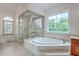 Bright bathroom features a glass-enclosed shower with decorative etching and a large soaking tub by the window at 5625 Crystal Harbor Ln, Hollywood, SC 29449