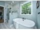 Bright bathroom with freestanding tub, glass enclosed shower, patterned tile floor, and view of the lush backyard at 1375 Tannanger Trl, Awendaw, SC 29429