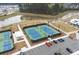 Aerial view of tennis courts with blue playing surface, parking lot, and the wooded neighborhood around at 716 Triangle Ln, Summerville, SC 29486