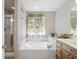Well lit bathroom with a soaking tub, window with leafy curtains, and wood cabinets at 9019 Parlor Dr, Ladson, SC 29456