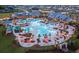 Aerial shot of a community pool with a splash pad, slide, lounge chairs, and tables with shade umbrellas in a Primary-planned community at 104 Snow St, Summerville, SC 29486